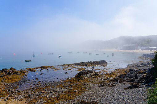 Blue sky begins to break through a low bank of coastal fog that sits over the fishing village of Porthdinllaen.