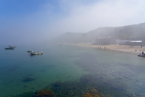 A summer afternoon and blue sky begins to break through a bank of heavy fog sitting over Porthdinllaen beach and village in Gwynedd, Wales