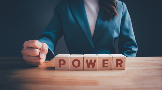 Businesswoman in green suit with fist gesture and wooden blocks cubes text POWER. Fist expressing force and power, girl power, teamwork and business decision concept.