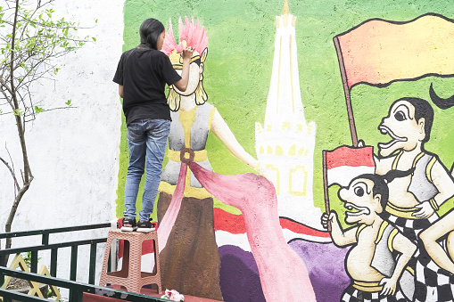 Yogyakarta, Indonesia - August 8, 2023: A female young artist is having a competition to draw a mural on the wall with the theme of the 78th Independence Day of the Republic of Indonesia.