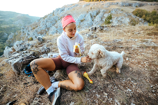 Hiking woman sits and eats a banana with her dog