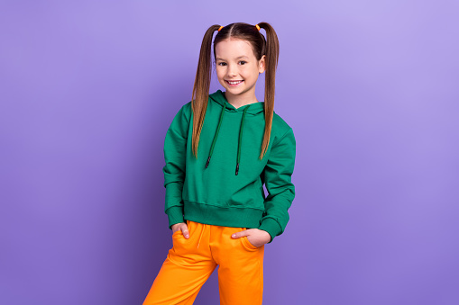 Photo of young girl brown hair ponytails wear sportive green sweatshirt posing for kids store clothes isolated on purple color background.