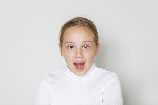 Portrait of surprised young girl with open mouth. Cute happy child looking at camera on white background. Surprise, idea and fun concept