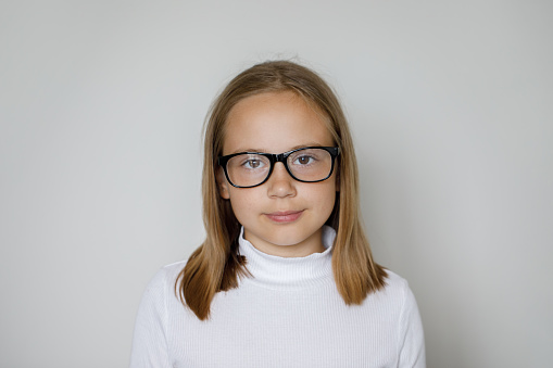 Clever child girl in glasses looking at camera on white background, studio portrait