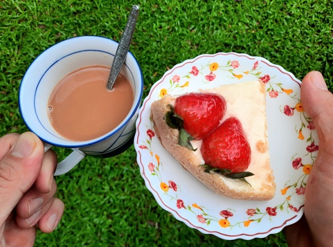 Hands holding Strawberry Cheesecake and Hot Milk Tea - Green background.