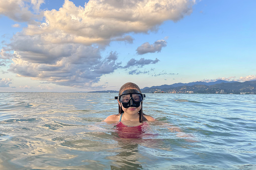Kid girl wearing snorkel mask in sea or ocean, happy holidays concept