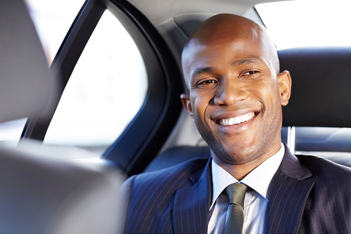 Happy African American male professional looking away while sitting in the back seat of car. Horizontal shot.