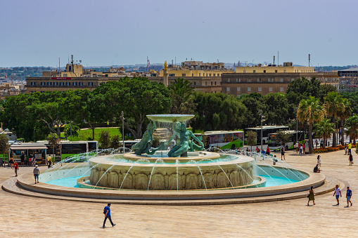 Valletta, Malta - August  8th 2019: The Triton Fountain in Triton Square with buildings in Floriana in the background.