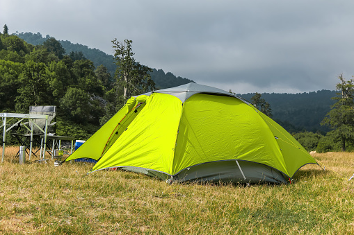 A relaxing holiday in nature with camping equipment, a green tent and the necessary materials in an empty area full of greenery and mountains.