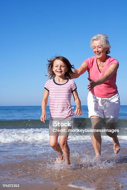 Grandmother Chasing Granddaughter Along Beach Stock Photo - Download Image Now - Beach, Grandmother, Grandparent