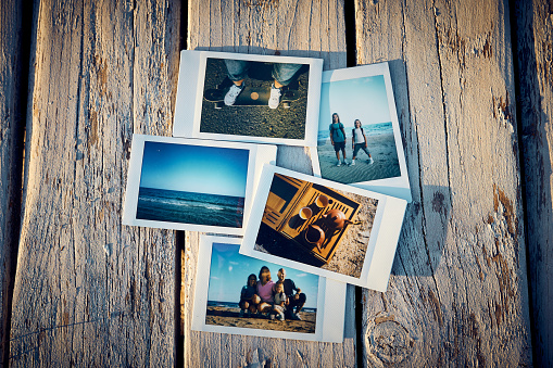 A several instant photographs lie on a old wooden table.