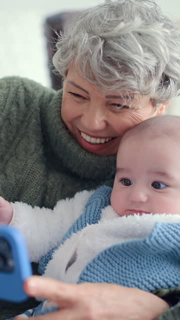 Happy, phone and grandmother with baby laughing while babysitting as love and care in a home and on social media. Internet, online and elderly woman bonding with child or grandchild in house together