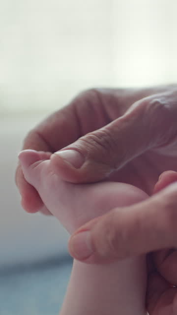 Hand, foot and a senior grandparent with a baby closeup in the home together for love or care as a family. Children, skin and an elderly person touching the sole of a newborn infant in a house