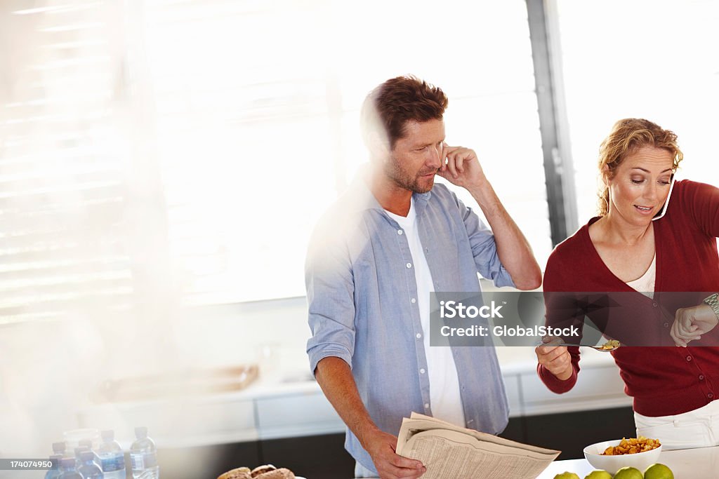 The stress of modern home life Mature couple in their kitchen going about their morning routine and running late Mature Women Stock Photo