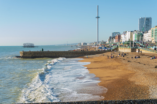 Brighton, UK - November 13th 2022: White waves on Brighton beach with the Doughnut Groyne, i360 Observation Tower and the derelict West Pier in the background.