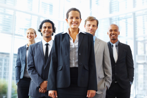 Happy mature business leader standing with crossed arms in front of her team in the office and looking at camera.