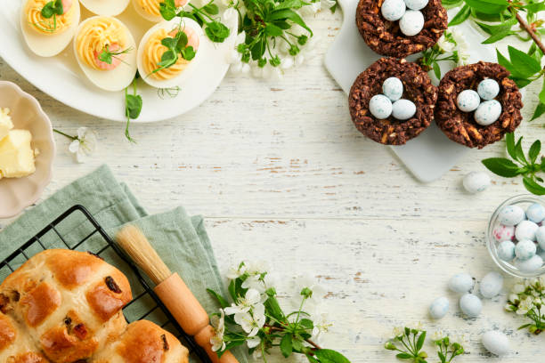 istock Easter brunch or breakfast. Easter chocolate nest cake with chocolate candy eggs, traditional hot cross buns and deviled eggs with bouquets of blooming apple trees. Spring Easter holiday food concept. 1740760198