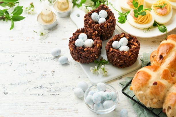 istock Easter brunch or breakfast. Easter chocolate nest cake with chocolate candy eggs, traditional hot cross buns and deviled eggs with bouquets of blooming apple trees. Spring Easter holiday food concept. 1740760914