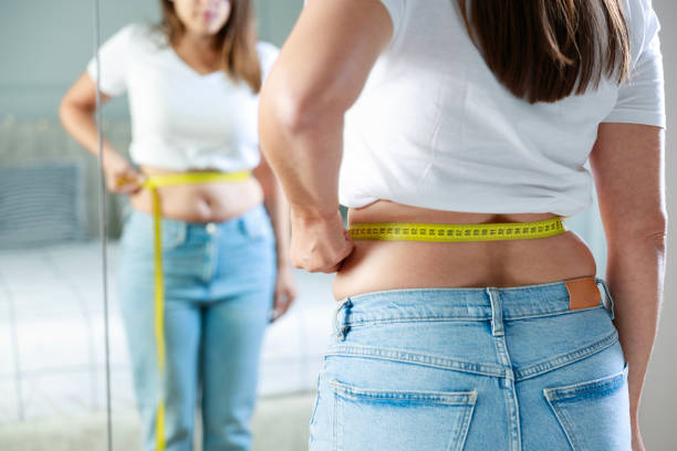 young woman taking measurements of her body in front of the mirror in her bedroom - fazer dieta imagens e fotografias de stock