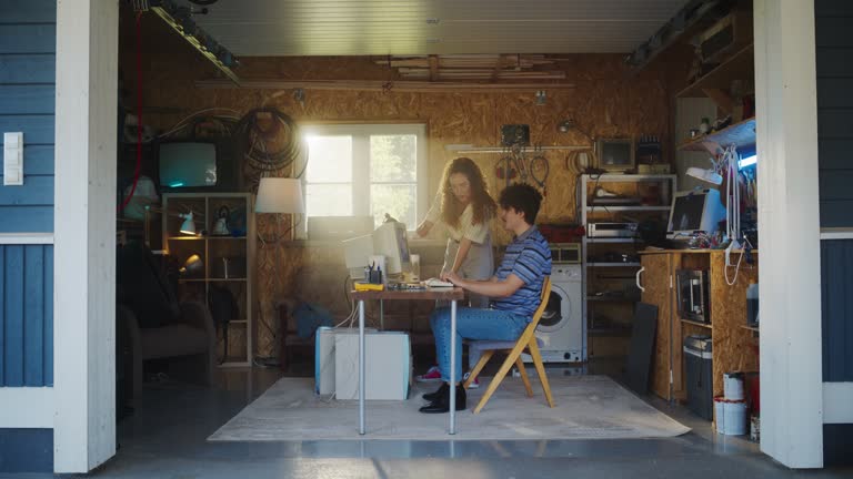 Caucasian Male Software Developer And Hispanic Female Designer Talking And Using Old Desktop Computer in Retro Garage. Diverse Startup Founders Working On Online Service In Nineties. Nostalgia Concept