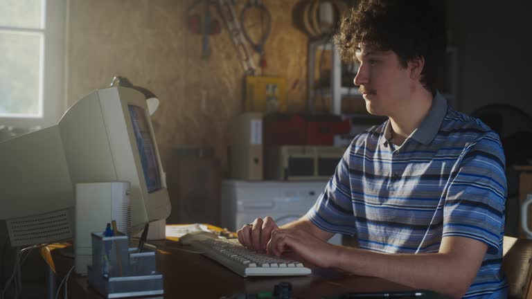 Caucasian Male Software Developer Programming On Old Desktop Computer In Retro Garage. Enthusiast Browsing Early Internet Forums, Coding Applications, Chatting Online In Nineties. Nostalgia Concept.