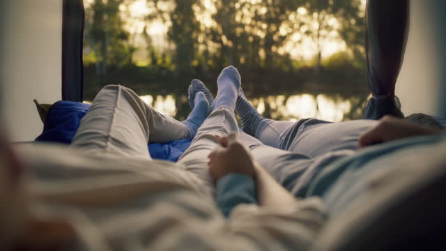 Feet, lying and couple holding hands in tent on camping trip, holiday or vacation in bonding, honeymoon or love. Woman, relax and man legs at campsite for travel break, nature or morning lake view
