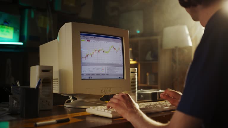 Caucasian Male Stock Trader Using Old Desktop Computer With Financial Candlestick Chart In Retro Garage. Man Analyzing Market Orders Before Entering Trade, Starting Investment Fund In Nineties.