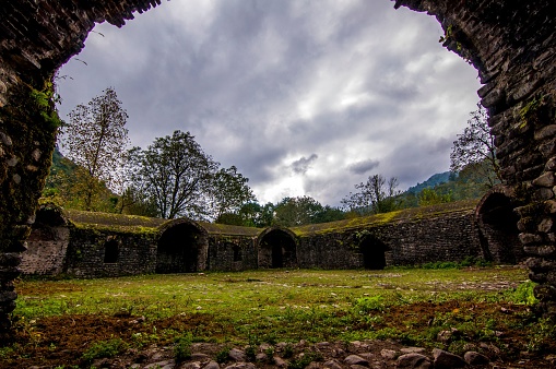 An abandoned stone tunnel leads the way down a path of overgrown grass, past crumbling ruins of a once-majestic structure