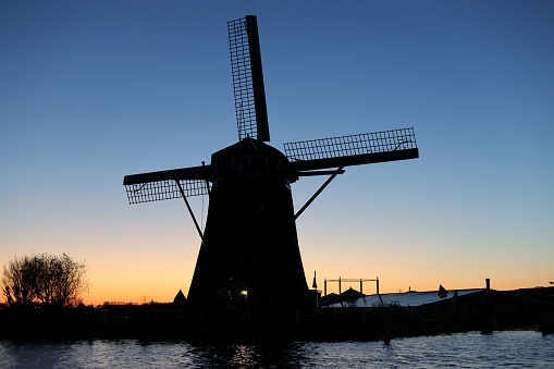 A majestic windmill illuminated in the sky as the sun sets over a tranquil body of water