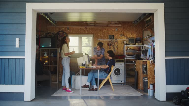 Diverse Team Of Three Young Startup Company Founders Working In Retro Garage, Using Old Desktop Computer. Male And Female Entrepreneurs Developing Innovative Fintech Service In Nostalgic nineties.