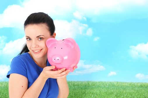 Young woman holding a piggybank outdoors with grass and sky