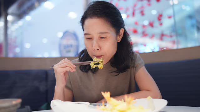 Asia woman fully immersed in the culinary journey of savoring deep-fried shrimp. Using chopsticks, expertly picking up a succulent shrimp and bringing it to mouth. Japanese food culture and tradition. Enjoys a hearty and satisfying Japanese meal happiness