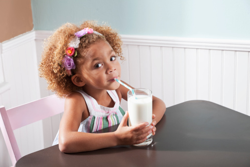 Cute little girl (4 years, mixed race), sitting at table with glass of milk