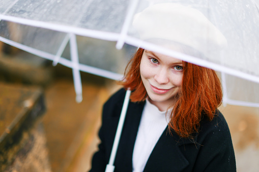 Girl rain umbrella. Happy girl portrait wearing a black coat with transparent umbrella outdoors on rainy day in park