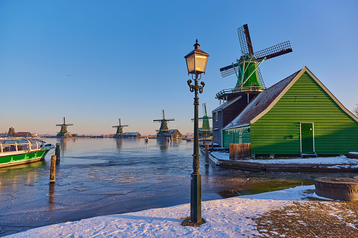 Zaanse Schans the historical village during winter, Netherlands. It’s early in the morning during sunrise. Everything is covered in snow and the water is frozen.