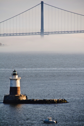 The George Washington Bridge emerges from a fog bank behind the Romer Shoal lighthouse (1898) off Sandy Hook, New Jersey at the entrance to New York Harbor.