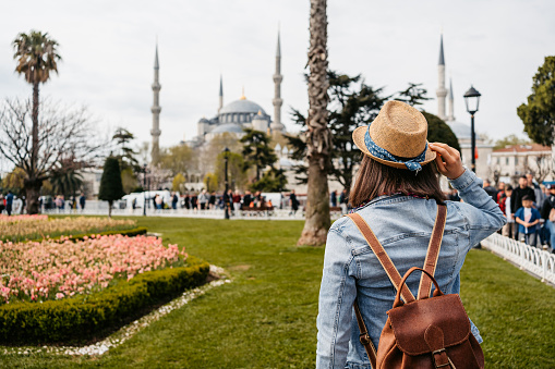 Young woman with a backpack standing in front of the Blue Mosque and enjoying the view in Istanbul, Turkey.