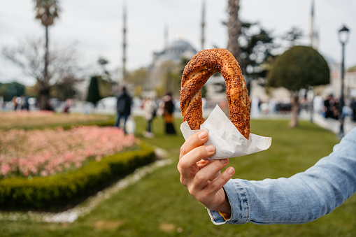 Woman holding a Turkish bagel (simit) in front of the Blue Mosque in Istanbul, Turkey. Close-up.