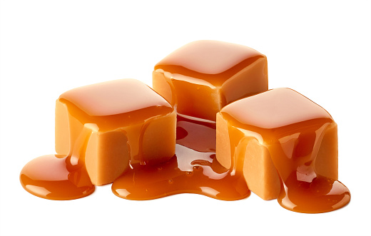 Three sweet caramel candy cubes topped with caramel sauce isolated on white background