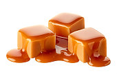 Three sweet caramel candy cubes topped with caramel sauce on white background