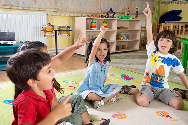 istock Group of preschool kids in classroom raising hands 174083655