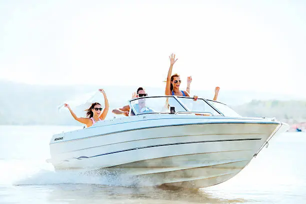 Group of young people with raised hands enjoying in a speedboat ride.