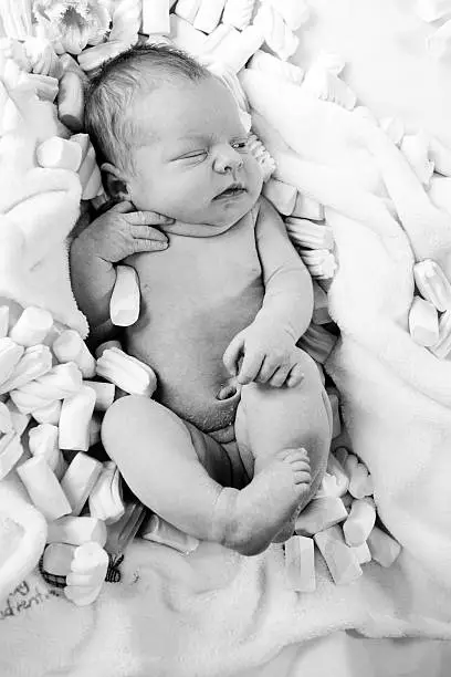 Only 6 days old girl is lying in the marshmallows. Black and white with soft light image.