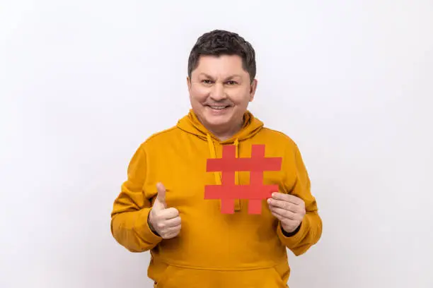 Photo of Man showing thumb up like gesture holding red hashtag sign, satisfied with target advertisement.