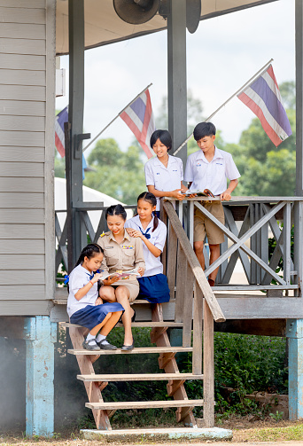 Vertical image of woman teacher teach and train her student in area of steps of the building with some student also look through the window and they look happy at school.
