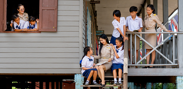 Woman teacher teach and train her student in area of steps of the building and they look happy at school.