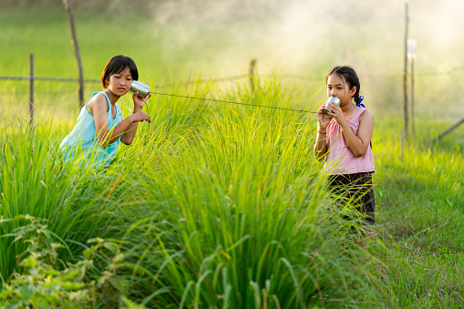 Side view two Asian young girls enjoy to play with can phone as toy in rice field with warm light and they look happy together.
