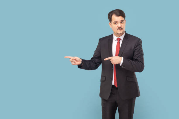 istock Serious man with mustache standing pointing aside at advertisement area, copy space for promotion. 1740855240