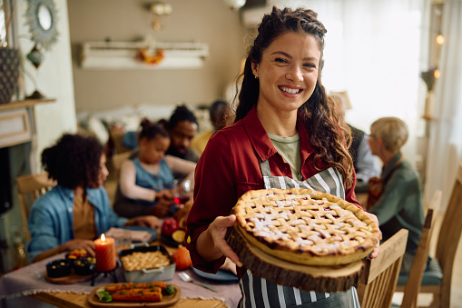 Happy woman serving sweet pie to her extended family on Thanksgiving and looking at camera.