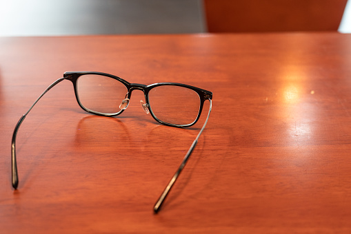 A classic design eyeglasses is placed on the wooden table. Resting from stress business working concept scene. Close-up at object and selective focus.
